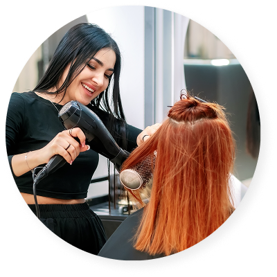 Hair stylist blow-drying and styling a client’s red hair with a round brush inside a salon.