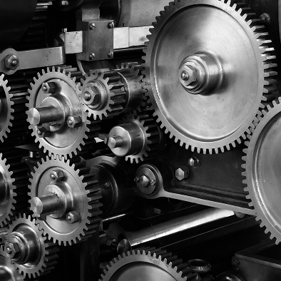 Close-up of interlocking metal gears and cogs inside industrial machinery, shown in black and white.