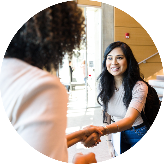 Smiling woman shaking hands with another person during a professional greeting in a bright indoor setting.